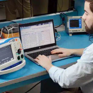 Mand bruger RescueNet DeviceDashboard software på laptop til at tjekke driftsstatus på defibrillatorer.